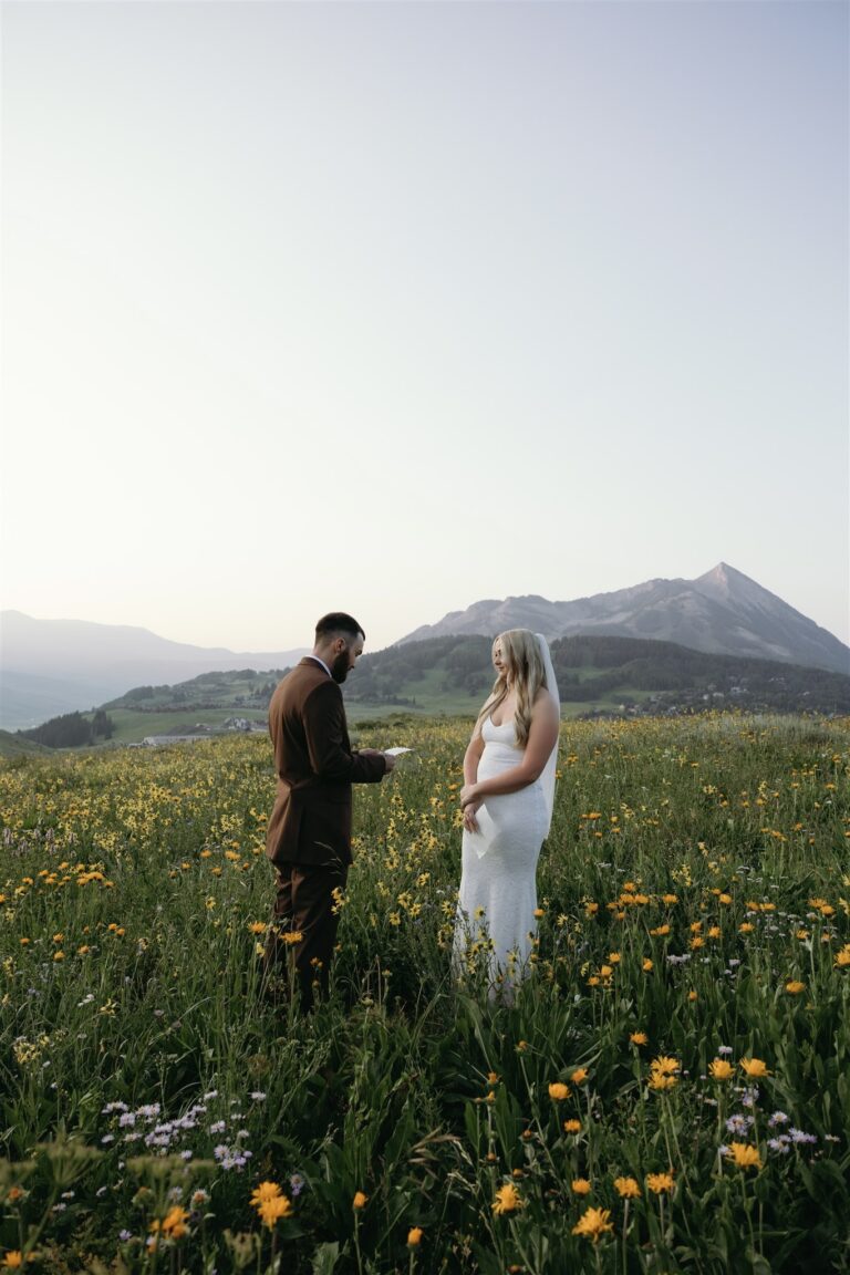 Groom shares vows with his bride in wildflower meadow near crested butte, Colorado