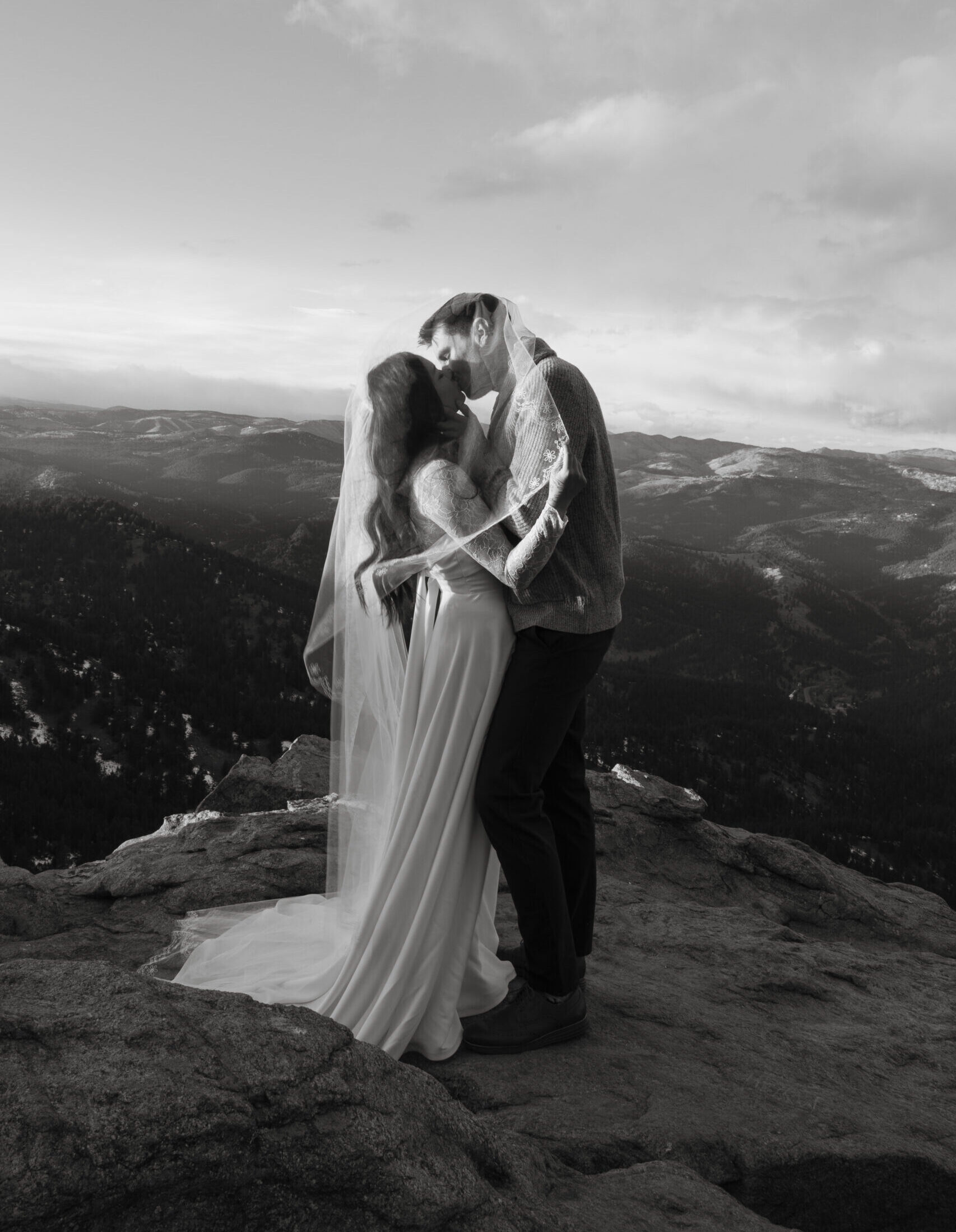 bride and groom share intimate kiss under veil on rocky outcrop of colorado mountains