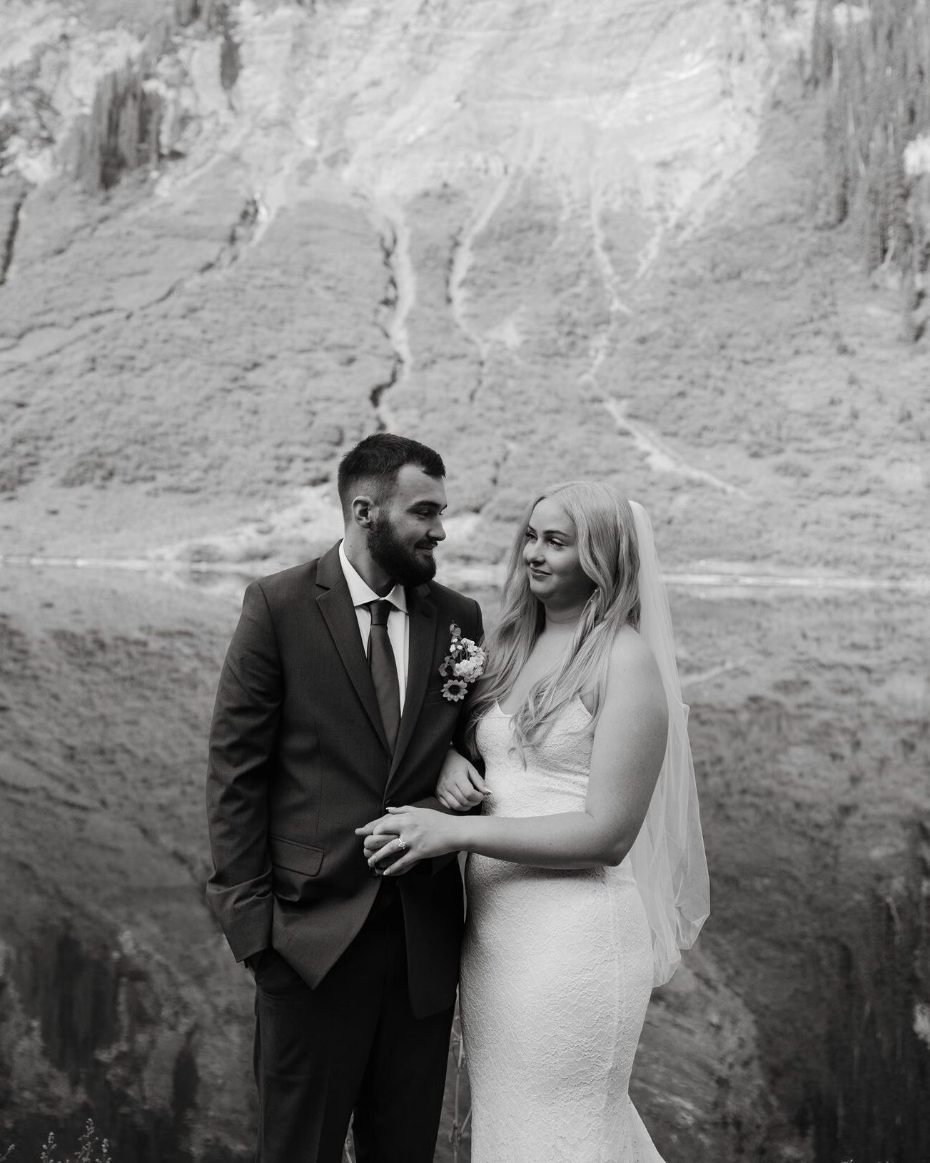 bride holds onto grooms arm in front of alpine lake in colorado during their intimate elopement