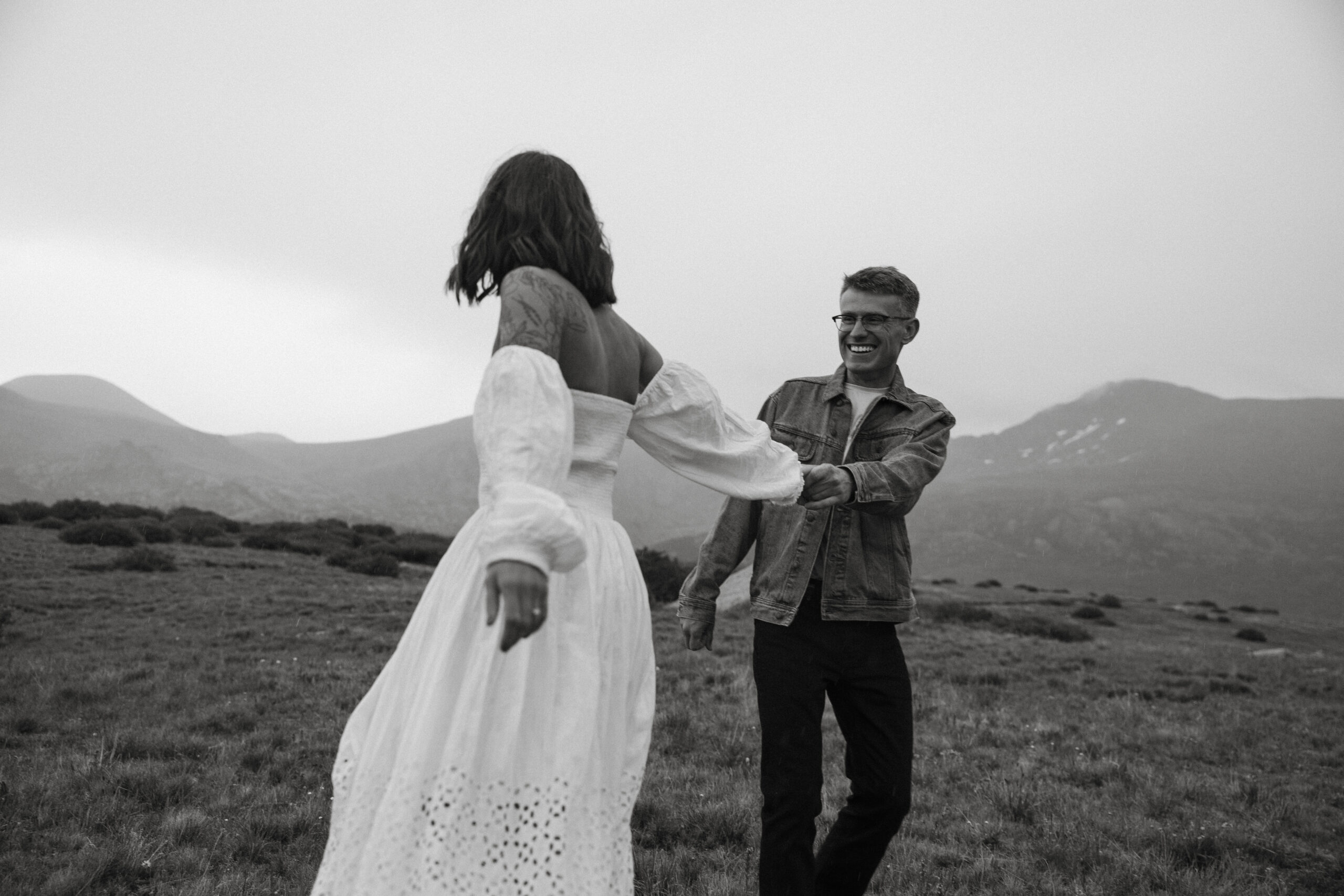couple dance playfully while holding hands with foggy mountains behind them