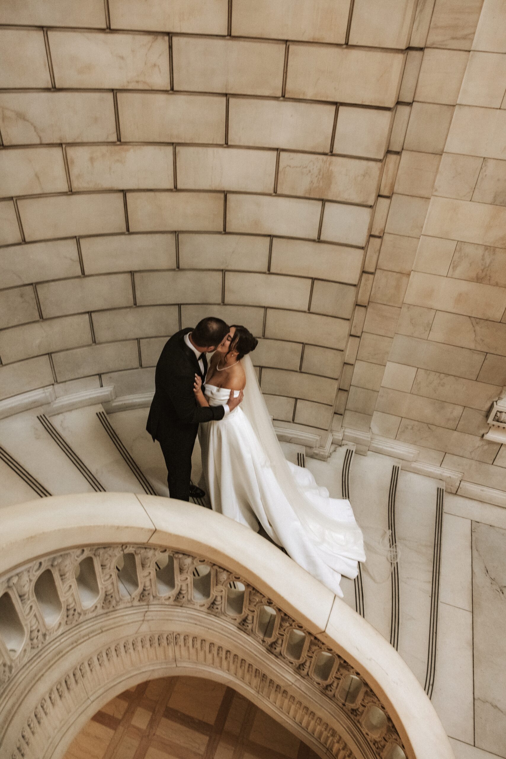 high angle of bride and groom meeting for a kiss on marble staircase during their fine art wedding