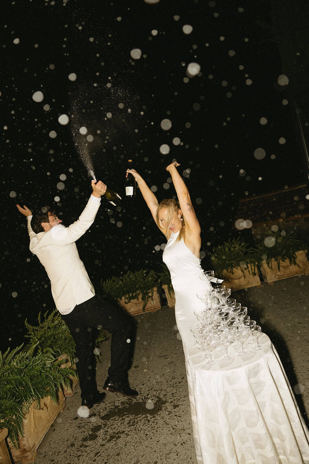 Newlyweds enjoying a fun celebratory moment popping champagne surrounded by bubbles and joyful cheers at a villa in Tuscany on their wedding day